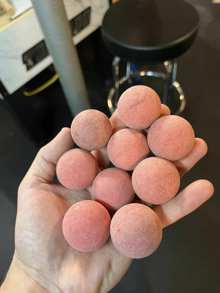 Hand holding 9 foosballs. The balls are greyish pink.