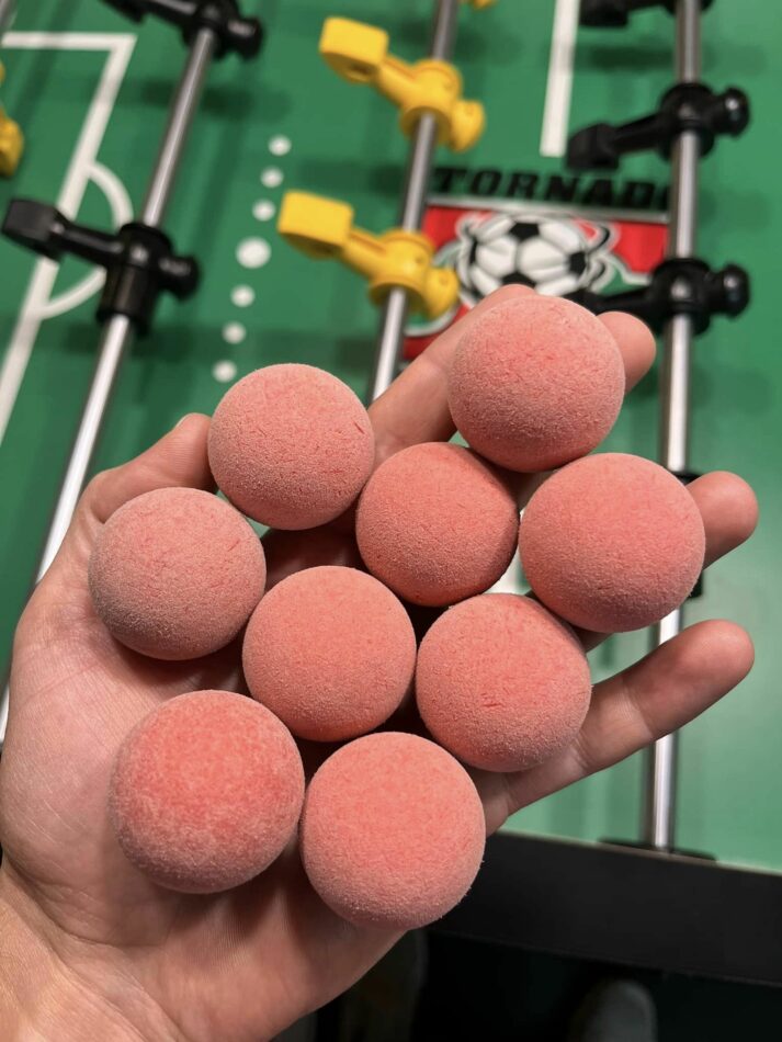 Hand holding 9 foosballs. The balls are fuzzy and a bright pink color.